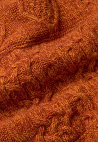 Tissu tricoté orange avec des motifs de câble complexes, montrant texture et profondeur en vue rapprochée.