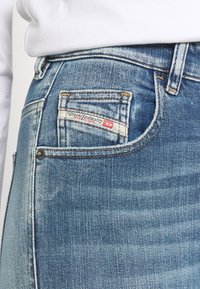 Blå denimjeans med en blekt tvätt, som har en bakficka med ett märkesetikett. Sömmen är synlig längs sömmarna.