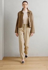 Brown leather jacket, beige pleated trousers, light ribbed top, and black floral detail shoes. Smooth textures against a neutral backdrop.