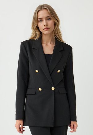 Blazer noir à double boutonnage en tissu lisse, doté de boutons dorés, de revers crantés et de deux poches avant. Silhouette ajustée.