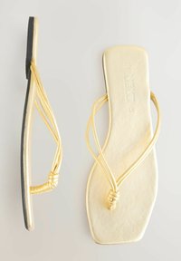 Guld faux läder flip-flops med en slät yta, platt sula och enkel knutdetalj på remmarna. Svart gummiyttersula för grepp.