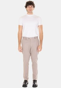 Pantaloni beige su misura con una texture liscia, caratterizzati da una vestibilità classica, pinces frontali e chiusura con bottone. Abbinati a una t-shirt bianca aderente.