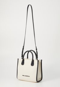 Sac en toile crème avec des accents en cuir noir, double poignées et une bandoulière amovible. Logo sur le devant.