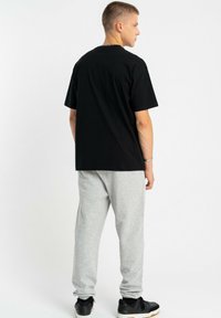 Czarna bawełniana koszulka, krótki rękaw, luźny krój, w połączeniu z jasnoszarymi spodniami dresowymi, elastyczne mankiety i czarne buty sportowe.