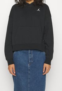 Sudadera negra corta con capucha y bolsillo canguro, con el logo Jumpman blanco en el pecho. Tela gruesa y puños acanalados. Combinada con una falda vaquera.