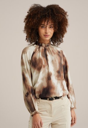 Blusa a fantasia marrone e crema con collo alto e maniche lunghe, realizzata in un tessuto liscio. Abbinata a una cintura nera.
