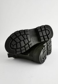 Bottes noires imperméables avec une semelle texturée, dotées d'un motif de tread robuste et d'un matériau supérieur lisse. Le design est minimaliste et fonctionnel.