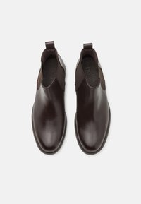 Hnědé kožené kotníkové boty s elastickými postranními panely a poutky na ztažení. Hladký povrch, zaoblený tvar špičky a jemné detaily prošívání.