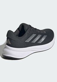 Baskets noires avec tige en mesh, dotées de trois rayures argentées. Semelle en caoutchouc blanche avec un design texturé, offrant traction et soutien.