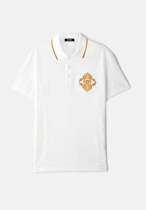 Camisola polo branca feita de algodão com detalhes em cor laranja no colarinho, apresentando um desenho em bordado dourado do brasão no lado esquerdo do peito.