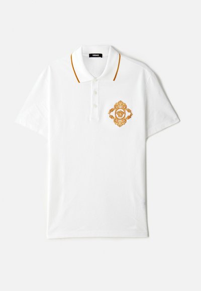 Fehér pamut póló narancssárga gallér részletekkel, bal mellkason hímzett arany címerrel.