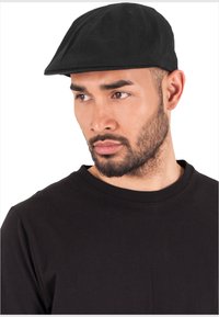 Black flat cap made of fabric, featuring a curved peak and seamless design. Worn with a black crew-neck t-shirt.