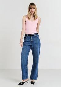 Top a fiori di ciliegia aderente, jeans blu a vita alta, cintura nera e tacchi a punta neri con accenti argentati. In piedi contro uno sfondo neutro.