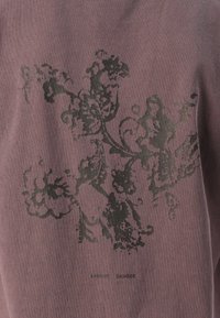 Sweatshirt en coton mauve foncé mettant en avant un motif floral noir et une texture subtile. Logos imprimés près du bas.