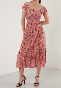 Vestido floral rosa con mangas cortas de volantes, corsé ajustado y falda en capas. Acompañado de sandalias negras de tacón alto.