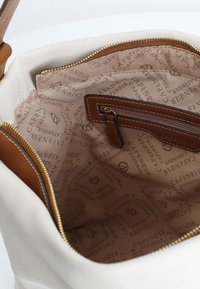 Interior de un bolso de lona con forro marrón claro que presenta un patrón de logotipos repetido. Bolsillo con cremallera en cuero marrón con una etiqueta de tela.
