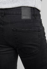 Černé džínové kalhoty s zadní kapsou, koženou štítkem na pasu a mírným ohrnutím na okrajích kapes.