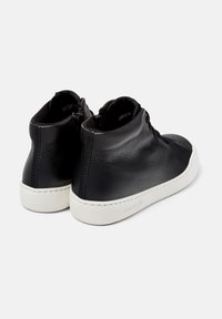 Zapatos altos de cuero negro con suelas de goma blanca, que cuentan con un cierre de cremallera y detalles de costura a lo largo de los lados. Textura suave, diseño minimalista.