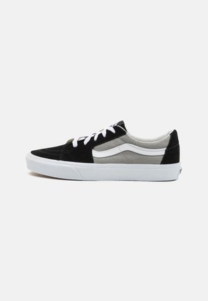 Sneaker in camoscio nero e grigio con lacci bianchi e strisce laterali. Presenta una suola piatta in gomma bianca e un design superiore texturizzato.