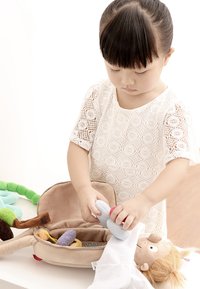 Plush toy storage bag in beige fabric, with colorful soft toys inside. A child is placing a soft, round toy into the bag.