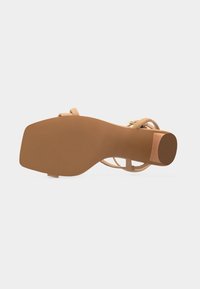 Πέδιλο με τετράγωνη σόλα, τακούνι μπλοκ και λεπτά μπεζ λουράκια, εμφανιζόμενο από κάτω σε απλό φόντο.