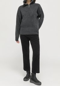 Mörkgrå höghalsertröja med halvdragkedja och ribbad textur, i kombination med svarta kordfläskbyxor och svarta snörkängor.