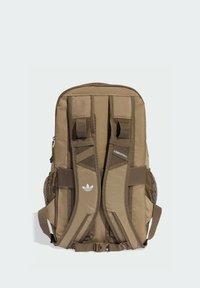 Brązowy materiałowy plecak z siateczkowymi, wyściełanymi paskami, regulowanymi klamrami oraz białym logo. Posiada wiele przegródek do przechowywania.