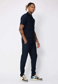 Chemise à manches courtes bleu marine et pantalons cintrés assortis en tissu lisse, accompagnés de baskets bicolores avec des accents noir, blanc et bleu.