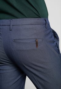 Námořnické modré kalhoty s texturou a jemným vzorem, s elegantním designem a zadní kapsou se značkovým akcentem.