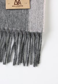 Écharpe en laine grise avec des franges, présentant un motif tartan dans des tons de gris foncé et de gris clair. Étiquette attachée à un coin.
