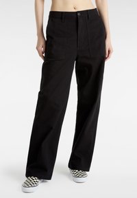 Svarta vida byxor gjorda av slitstark tyg, med framfickor och knäppning. Tillämpade med rutiga slip-on skor.