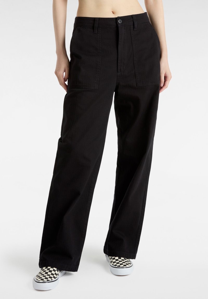 Svarta vida byxor gjorda av slitstark tyg, med framfickor och knäppning. Tillämpade med rutiga slip-on skor.