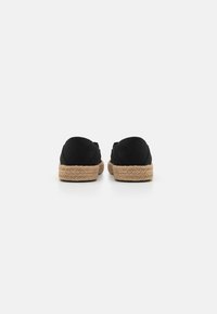 Des chaussures espadrilles noires avec une semelle en jute tissée. Tige en tissu doux avec un dos arrondi et un design minimaliste, adapté à un usage décontracté.