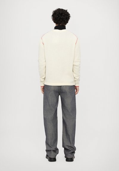 Hvid sweater med lyserøde detaljer, tætsiddende ærmer og ribbet kant. Kombineret med løse, mørkeblue denim bukser og sorte støvler.