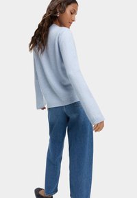Jasnoniebieski sweter dziany z długimi rękawami i prążkowanymi mankietami, w połączeniu z luźnymi niebieskimi dżinsami. Miękka tekstura i swobodny fason.