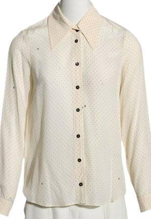 Cremefarvet bluse med lange ærmer med små sorte prikker, spids krave og sorte knapper foran, vist på en mannequin.
