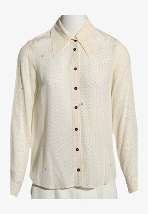 Cremefarvet bluse med lange ærmer med små sorte prikker, spids krave og sorte knapper foran, vist på en mannequin.