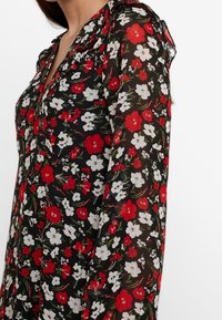 Svart genomskinlig klänning med blommönster som har röda, vita och gröna blommor. Volangkrage och långa ärmar. Elegant design.