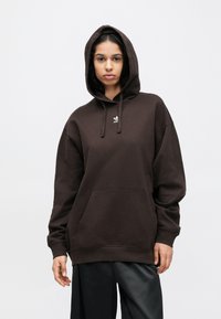 Καφέ φούτερ με κουκούλα και μεγάλο μπροστινό τσέπη, κουκούλα με κορδόνι και μικρό λευκό λογότυπο στο στήθος. Μαλακή υφή και άνετη εφαρμογή.
