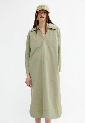 Robe vert olive clair avec un col et des manches longues. Tissu lisse ; présente une patte de boutonnage à l'avant et un subtil détail de logo.