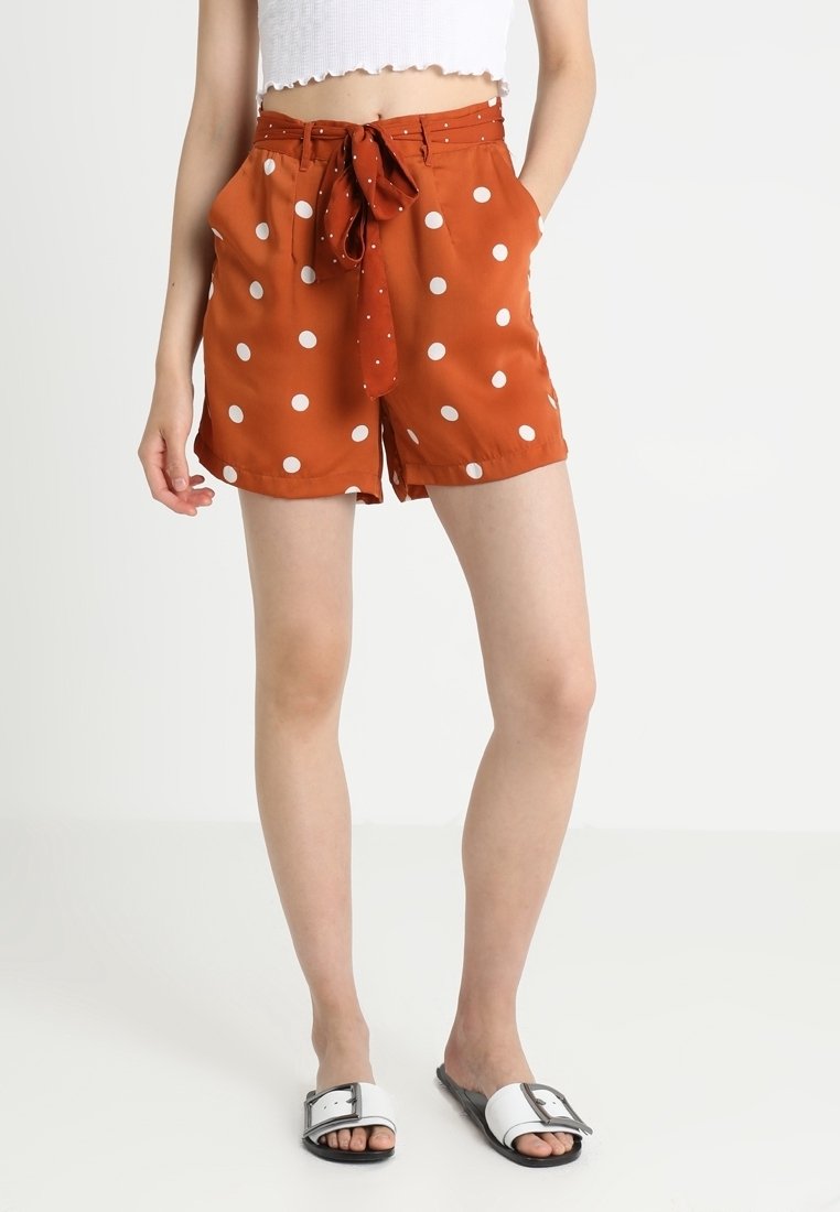 Pantaloni corti arancioni con pois bianchi, dotati di vita legata e tasche laterali. Realizzati in un tessuto leggero con una superficie liscia.