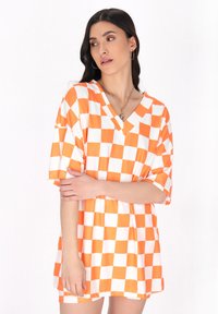Orange og hvid ternet oversized T-shirt med V-udskæring og korte ærmer, lavet af blødt stof med en afslappet pasform.