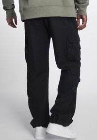 Černé cargo kalhoty s několika bočními kapsami, elastickými manžetami a volným střihem. Vyrobené z odolné látky, navržené pro praktičnost.