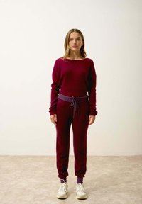 Bordowy sweter dzianinowy i dopasowane joggery z fioletowym sznurkiem. Gładka faktura, luźny krój, elastyczne mankiety i ściągacze przy kostkach.