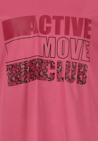 Lyserød t-shirt med fed sort skrift "ACTIVE MOVE CLUB" og en seksjon med hjerte mønster. Lavet af blødt, let materiale.