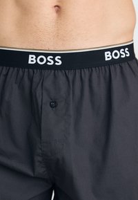 Shorts gris avec une taille élastique noire affichant le logo "BOSS" en blanc. Comprend un bouton et une texture de tissu douce. Design à l'avant plat.