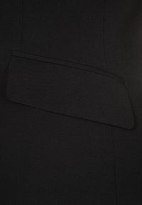 Tissu de robe noire avec un accent de rabat structuré et superposé sur le côté gauche, texture lisse avec une apparence sur mesure.