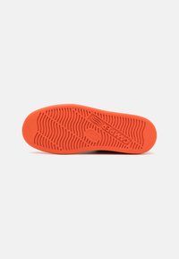 Semelle de chaussure en caoutchouc orange avec un motif de bande de roulement ondulé, comportant un logo et une surface texturée pour une meilleure adhérence.