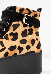 Anklesukk leopard print med myk, pelsaktig tekstur, svart suedestroppe med gullspenne og solid sort plattformsåle.