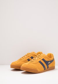 Sneaker in suede giallo con strisce blu navy, suola in gomma testurizzata e design a punta rotonda. I lacci e il colletto imbottito completano il look.